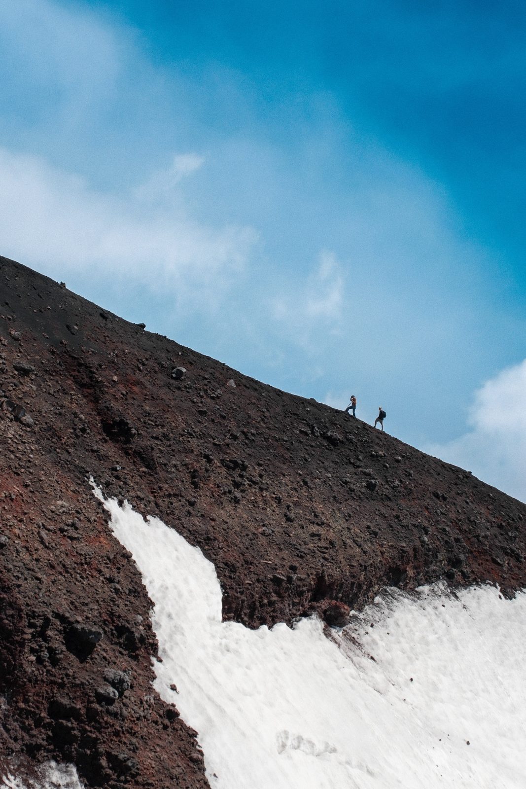 Two hikers on a volcanic ridge of Mount Etna